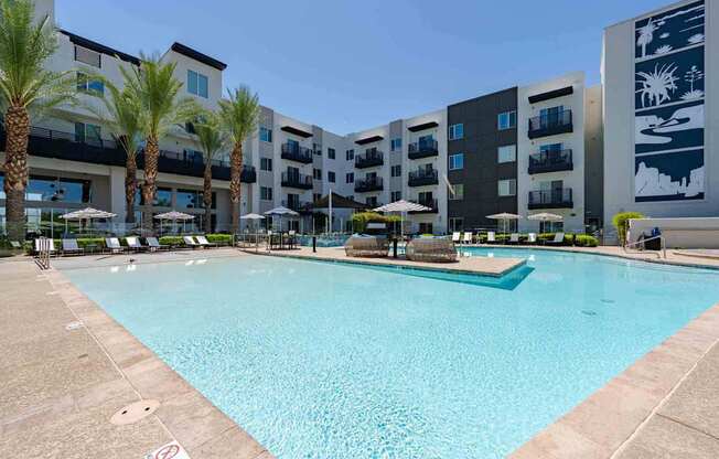a large swimming pool with umbrellas and chairs in front of an apartment building