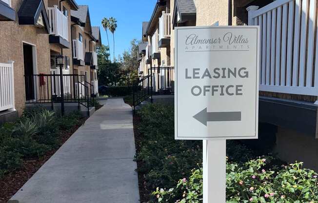 A sign for a leasing office is on the right side of a walkway.