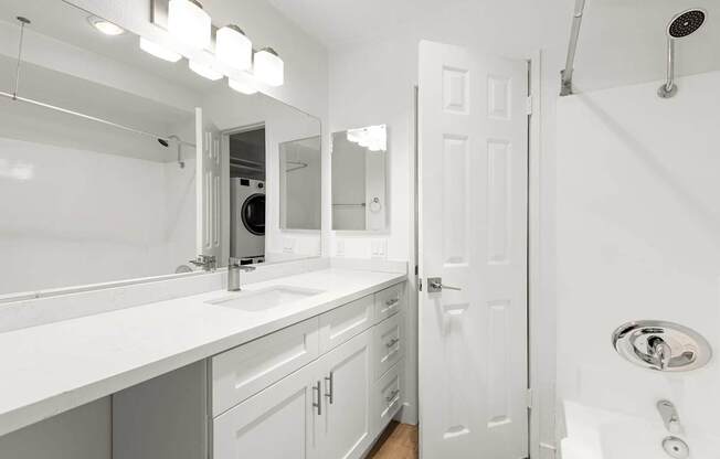 A white bathroom with a sink, mirror, and shower.