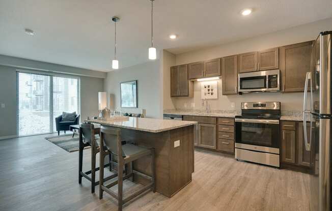 Kitchen and dining room with chairs next to the island, light stone countertops, and dark brown cabinets