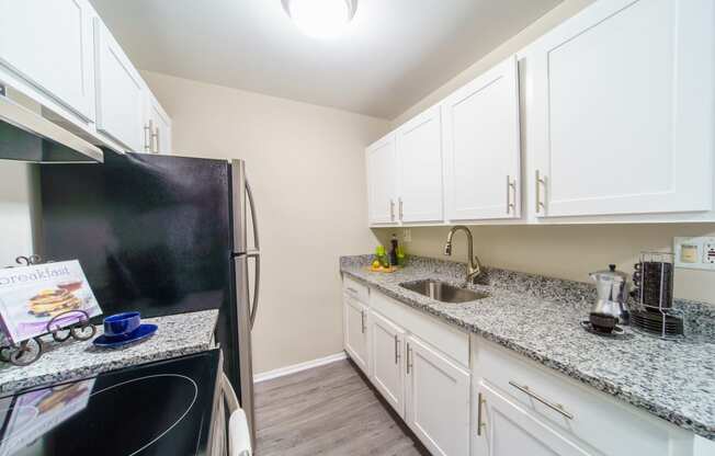 Grey hardwood like flooring with white cabinets, stainless steal appliances, and grey and white stone counter tops.