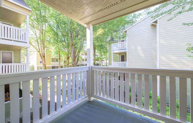 A white balcony with a railing overlooking a green area.