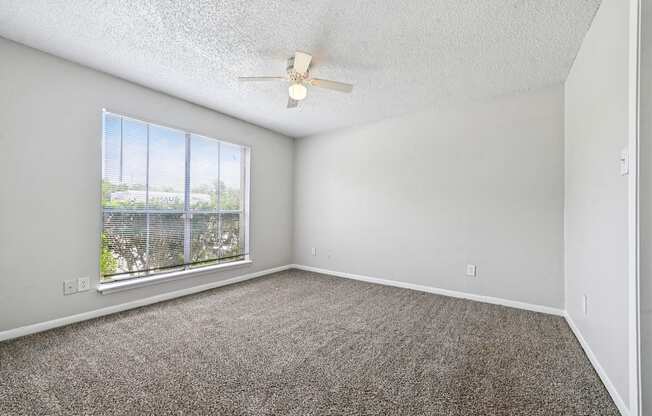 A room with a ceiling fan and a window overlooking a fence.