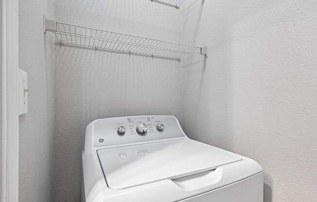 A white dryer is sitting in a small, white-walled laundry room.