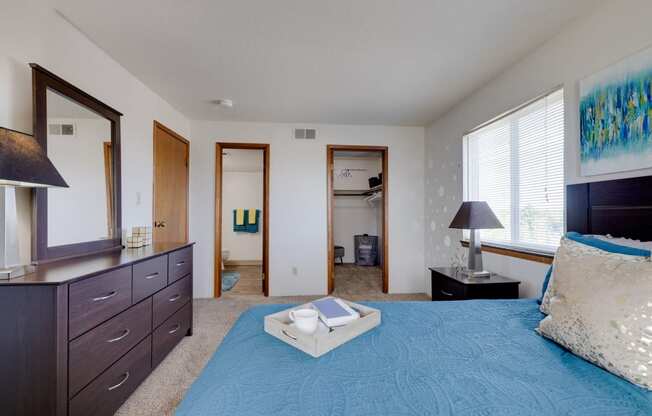 Bright bedroom in the two-bedroom model unit at Olde English Village, showcasing a large window and well-appointed furnishings.