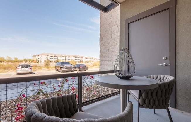 A balcony with a table and two chairs overlooking a parking lot.