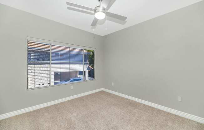 an empty bedroom with a large window and a ceiling fan