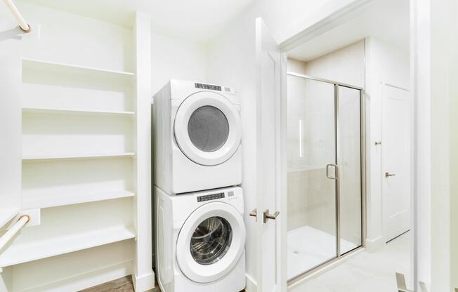 In-home laundry with stacked washer and dryer inside the primary closet features open shelving for efficient daily routines.