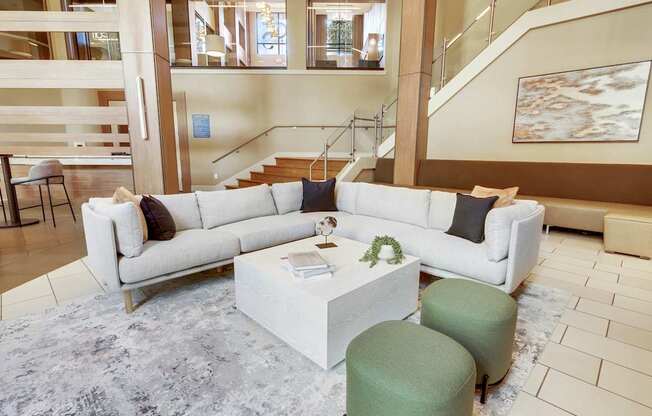 A white sofa with a green ottoman and a white coffee table in a spacious room.