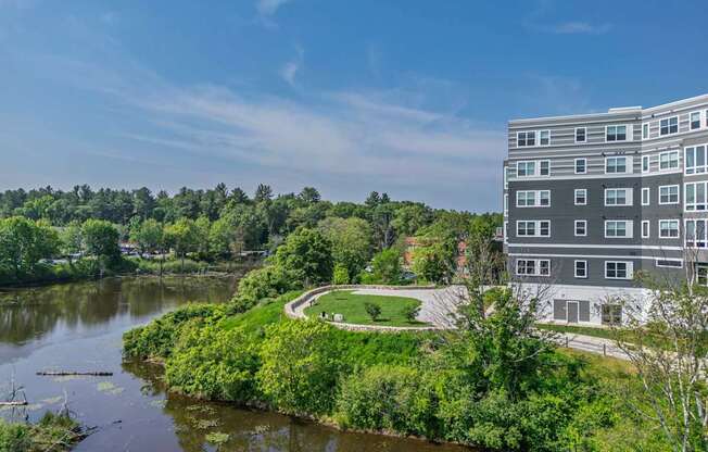 A modern building is situated by a body of water with a green area in front of it.