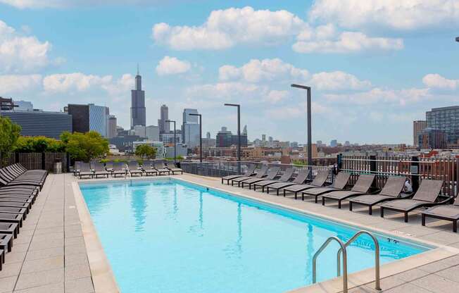 A swimming pool with lounge chairs and a city skyline in the background.