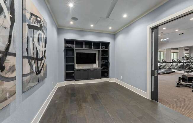 A spacious room with a large artwork on the wall and a view of a gym through the open door.