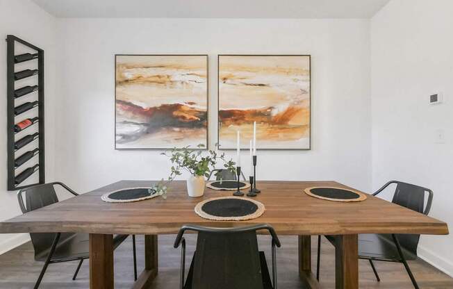 a dining room with a wooden table and two paintings on the wall