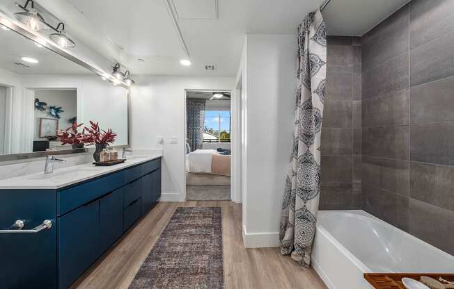 A bathroom with a blue vanity and a bathtub with a brown mat.