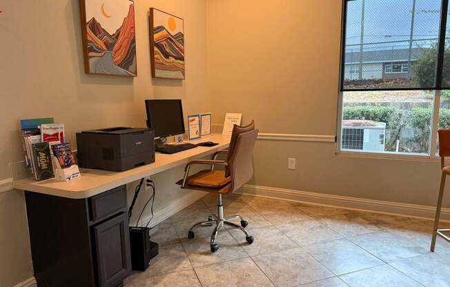 A room with a desk, chair, and two paintings on the wall.