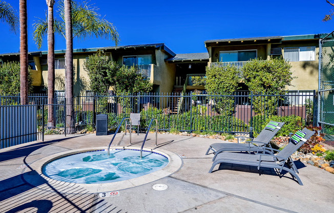 A pool with a hot tub in the middle of a concrete patio surrounded by chairs.