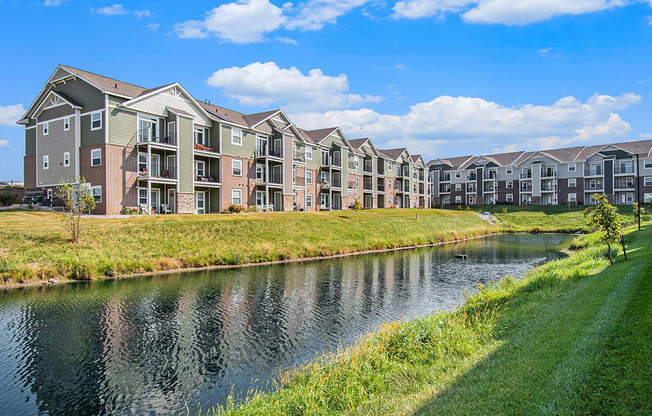 A modern apartment building situated next to a body of water at Strathmore Apartment Homes, West Des Moines, IA