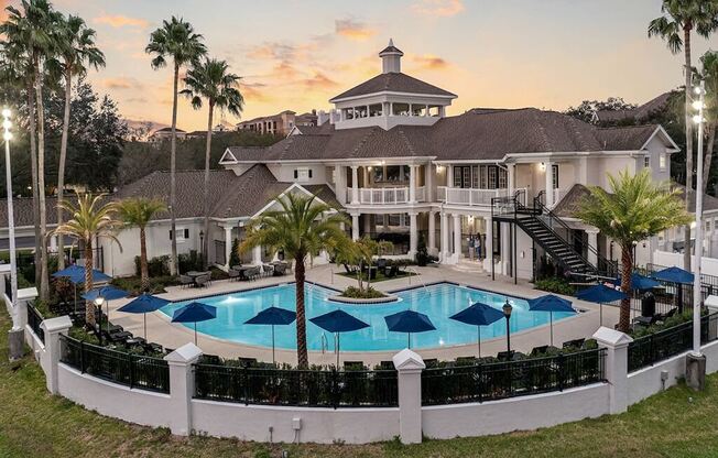 a clubhouse with a large pool and umbrellas at sunset
