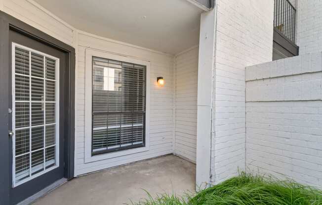 a patio with a black door and a window with venetian blinds