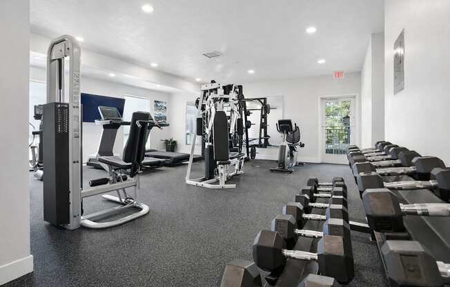 A gym with a variety of equipment including dumbbells, weight machines, and a treadmill.