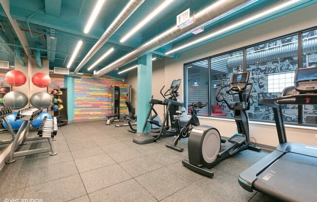 a gym with various machines and weights in a building with a large window