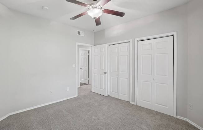 A room with a ceiling fan and three doors.
