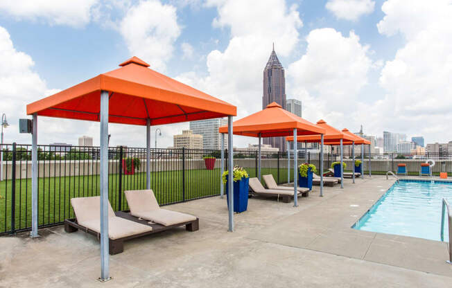 an outdoor pool with chairs and umbrellas and a city in the background