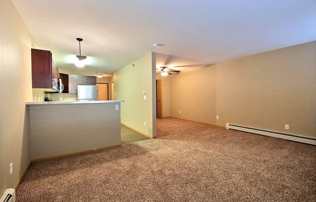 the living room and kitchen of an empty apartment with carpeting. Fargo, ND Urban Plains Apartments