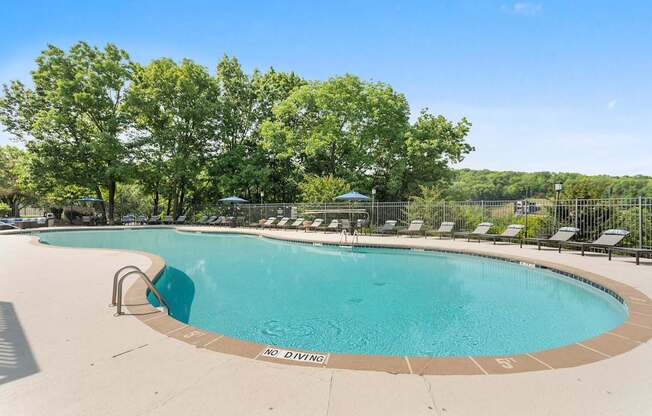 A large swimming pool surrounded by trees and lounge chairs.
