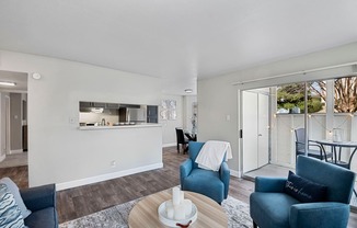 a living room with blue couches and chairs and a kitchen with a sliding door