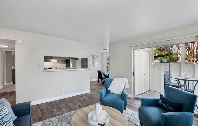 a living room with blue couches and chairs and a kitchen with a sliding door