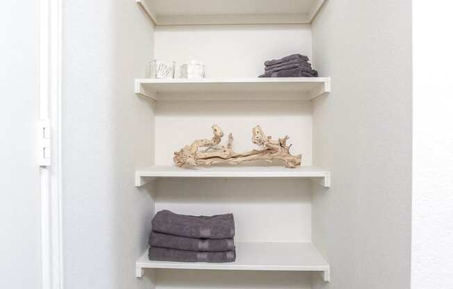 a small closet with white shelves and a basket on the floor