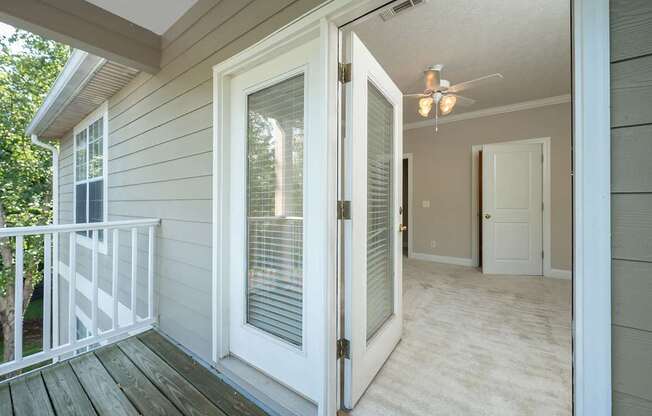 A white door with a window is open to a room with a ceiling fan.