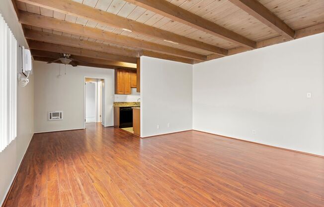 an empty living room with hardwood floors and a kitchen in the background