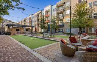 A patio with wicker chairs and a table is surrounded by apartment buildings.