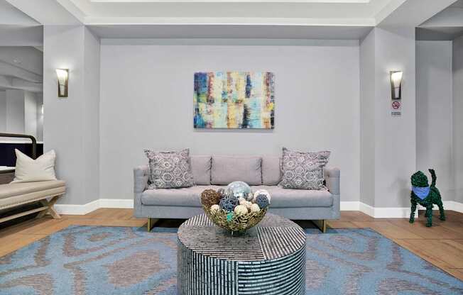 A living room with a grey couch, a coffee table, and a painting on the wall.