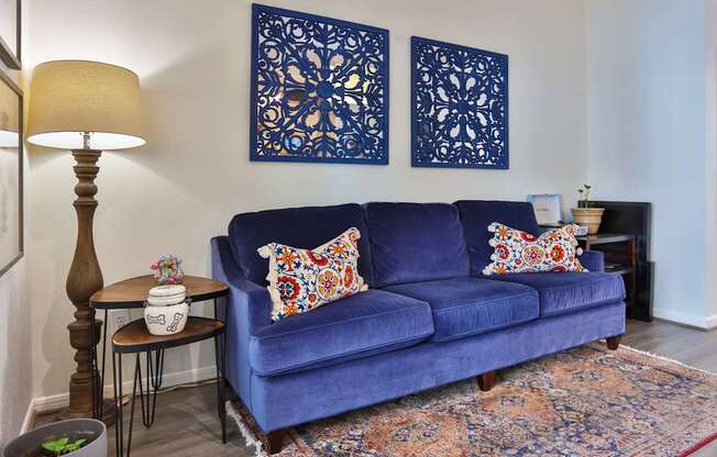 A resident lounge with a blue couch, lamp, and a side table at The Inverness Apartments in Houston, TX