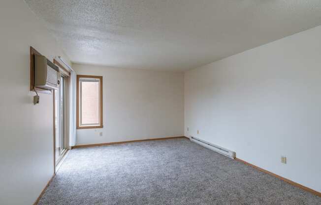 an empty living room with carpet and a window. Fargo, ND Crescent Park Apartments