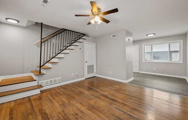 an empty living room with a ceiling fan and a staircase