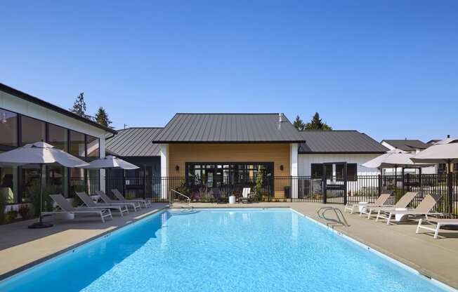 a swimming pool with lounge chairs and umbrellas in front of a building