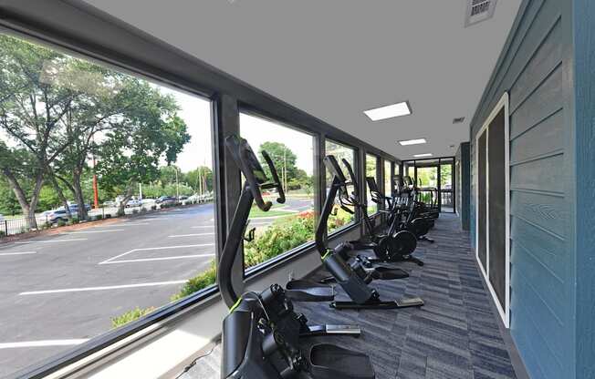 a row of exercise equipment in a gym with large windows