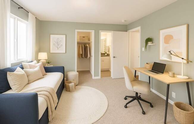 A room with a blue couch, a desk with a laptop, and a white chair.