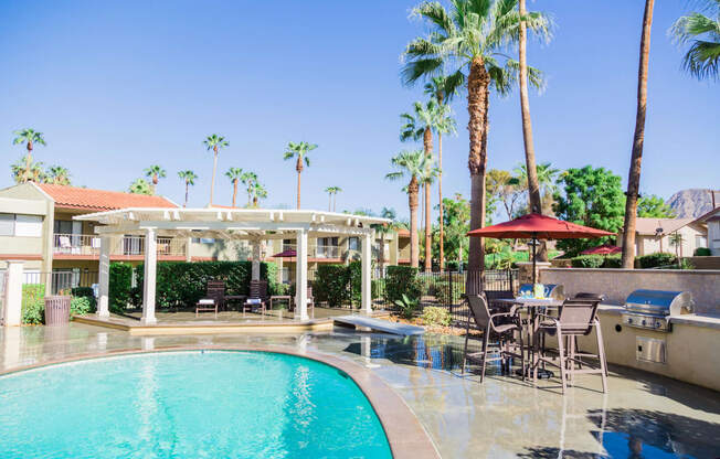 a resort style swimming pool with tables and chairs and palm trees