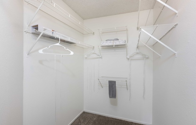 a walk in closet with white walls and shelves and hanging racks