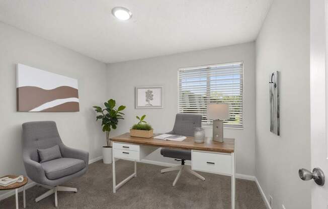 A room with a grey chair, a desk with a plant on it, and a painting on the wall.