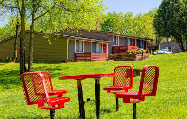 The Retreat at Indian Lake grounds with red steel mesh picnic table and chairs on green lawn with apartments in background.