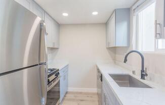 a white kitchen with a stainless steel refrigerator and sink at The Preston at Hillsdale, San Mateo, CA