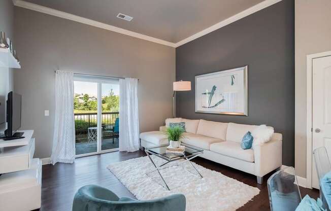 A living room with a white couch, a glass coffee table, and a painting on the wall.