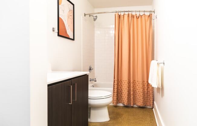 a bathroom with a white toilet next to a shower with an orange shower curtain at The Ferguson Apartments, Michigan, 48226