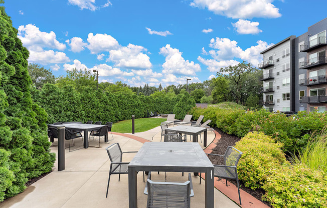 A patio with a table and chairs is surrounded by greenery.
